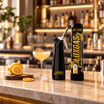 Botanical cocktail with orange, fresh herbs and an unbranded culinary cream whipper on a professional bar counter