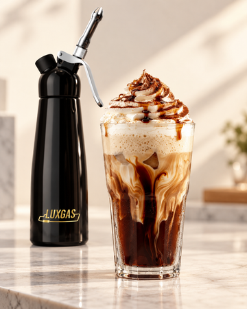 Coffee whipped cream served over an iced coffee beside a professional LUXGAS cream dispenser in a bright café setting