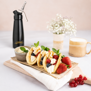 Fruit-filled pancakes topped with mascarpone whipped cream beside a LuxGas cream dispenser.