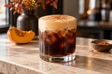 Glass of iced coffee topped with pale pumpkin cold foam and cinnamon