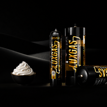 Food-grade nitrous oxide cylinders and silver cream chargers on a dark surface, B2B supply